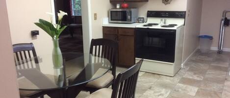 A kitchen with a glass dining table, wooden chairs, a microwave, an oven, and a trash can.
