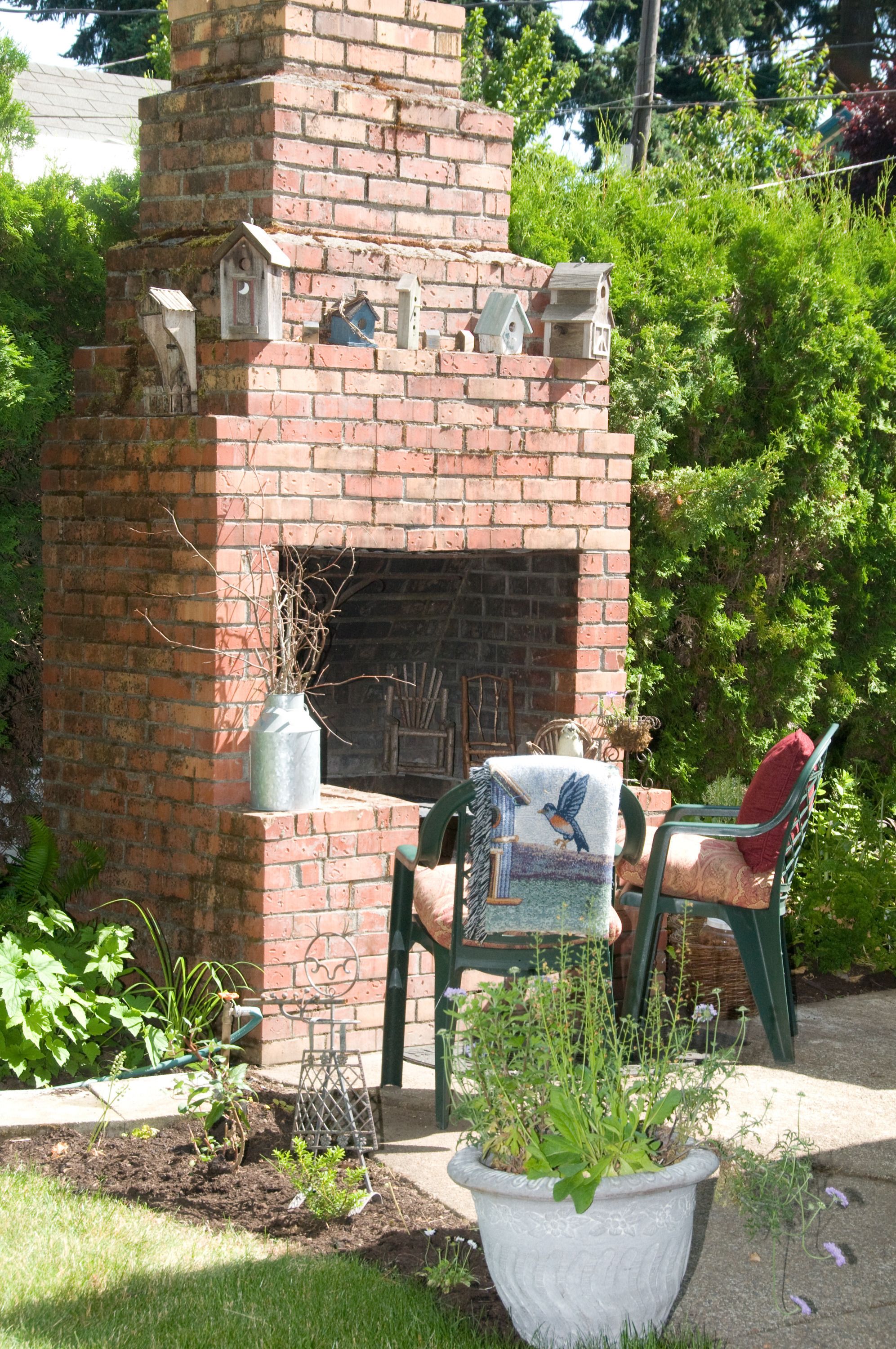 A brick fireplace with birdhouses, a potted plant, and a chair with a blanket.
