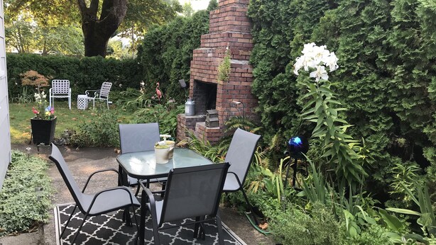 An outdoor patio with a brick oven, surrounded by lush greenery and a seating area with chairs and a table. - Kalmia Cottage (Junction City)