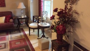 A living room with a red sofa, a small round table with a lamp, a chair, and a vase of flowers. - Kalmia Cottage (Junction City)