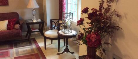 Un salon avec un canapé rouge, une petite table ronde avec une lampe, un fauteuil et un vase de fleurs.
