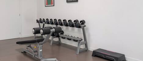 Un gimnasio con una prensa de banca, mancuernas y una plataforma elevada.