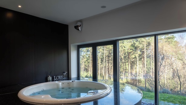 A modern bathroom with a large bathtub, dark marble flooring, and a view of a forest through large windows.