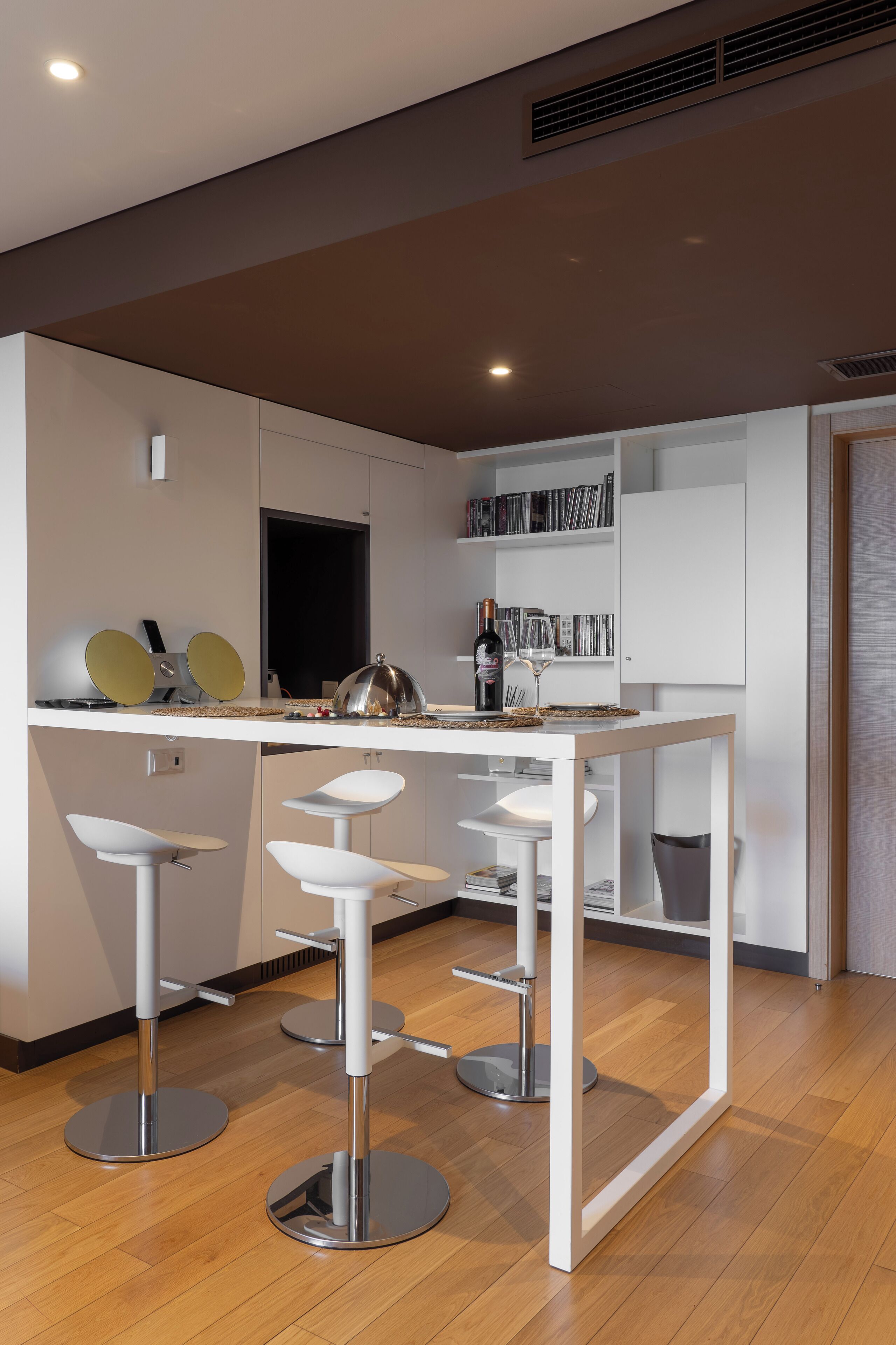 A modern kitchen with white cabinetry, a central island with stools, and a wine bottle.