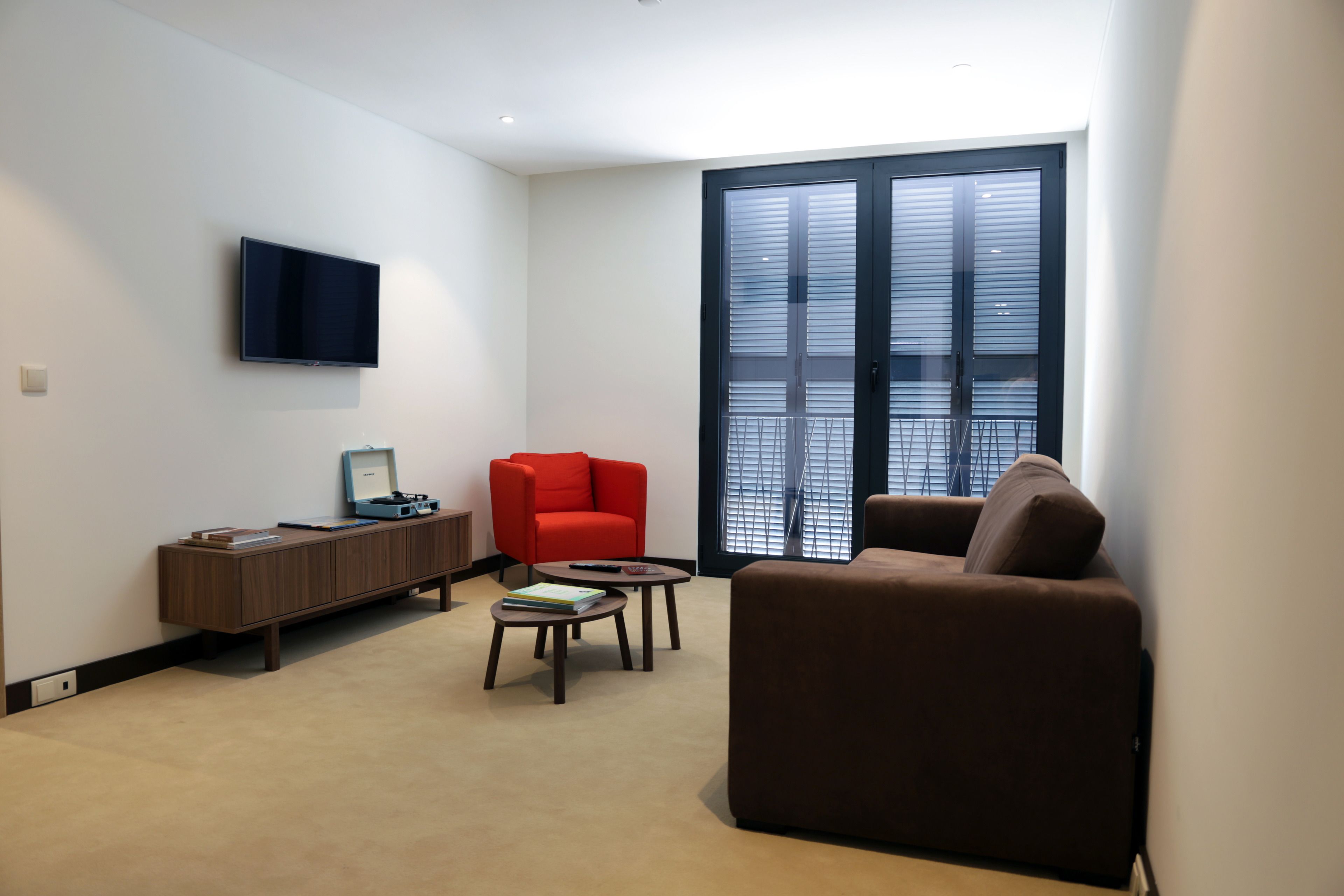 A modern living room with a flat-screen TV, a red armchair, a brown sofa, and a wooden cabinet.