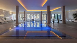 A modern indoor pool area with lounge chairs and a stone wall.
