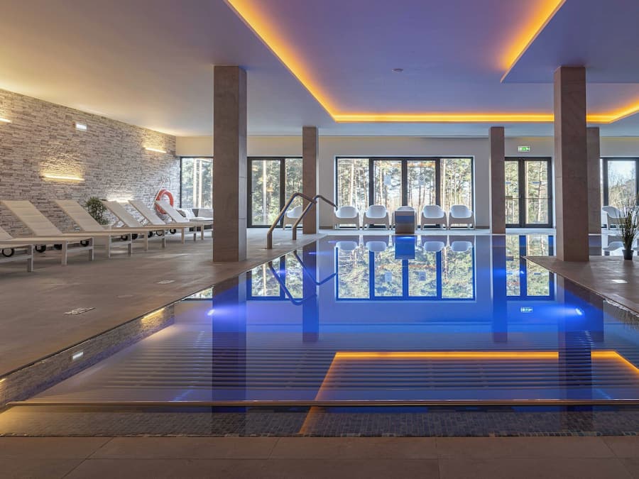 A modern indoor pool area with lounge chairs and a stone wall.