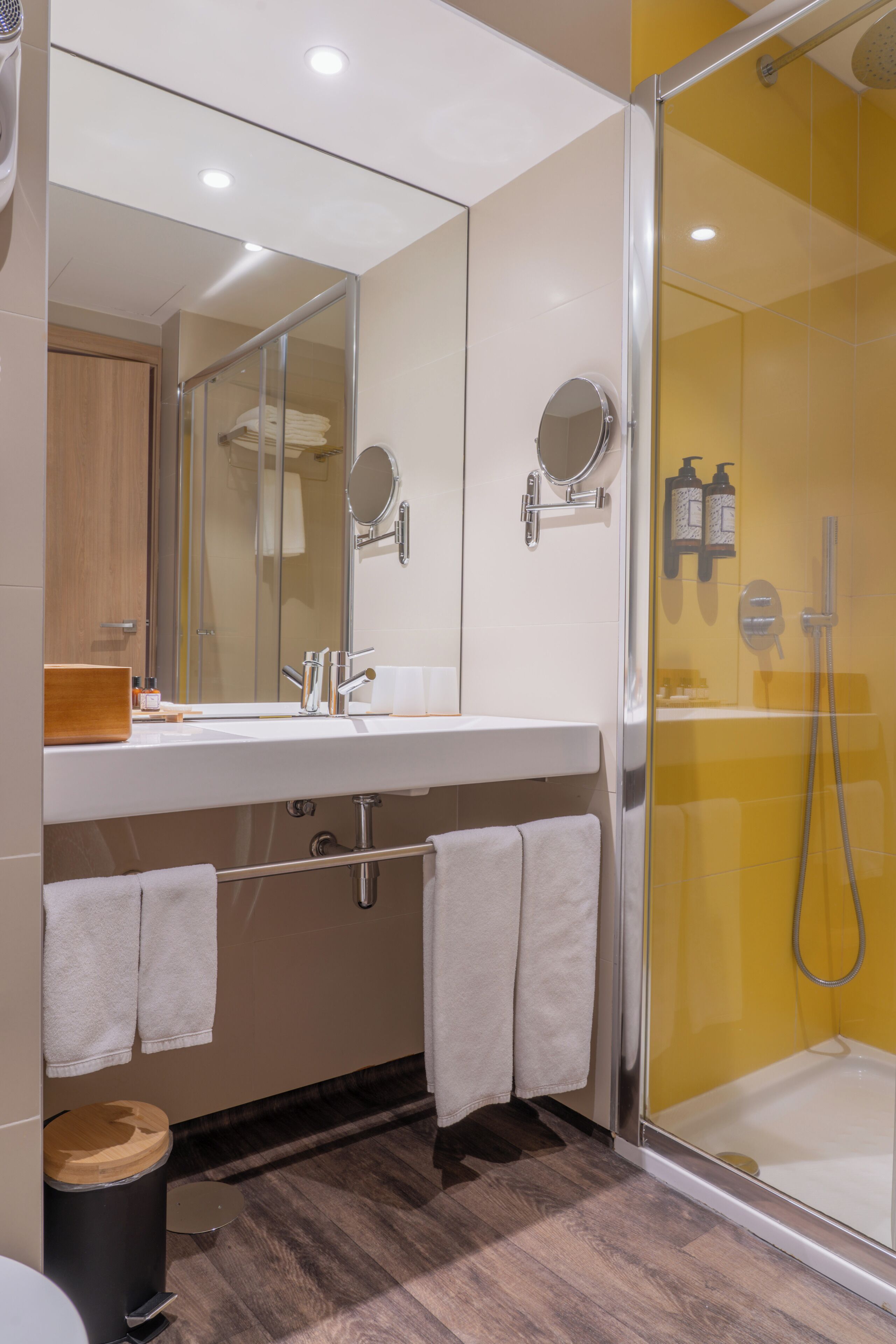 A modern bathroom with a glass-enclosed shower, a large mirror, and a wooden vanity.