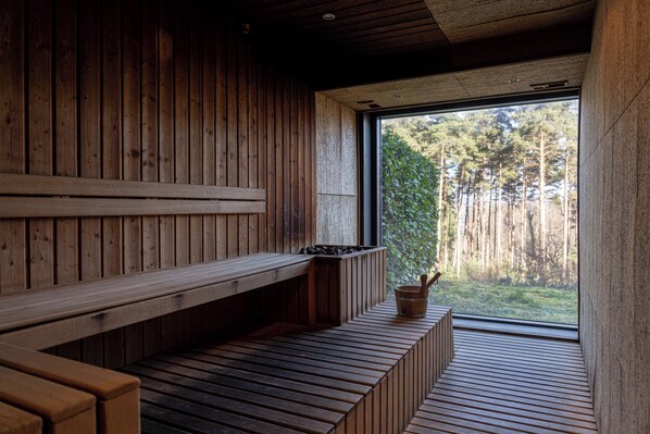 Una sauna con bancos de madera y un amplio ventanal con vistas a un bosque.