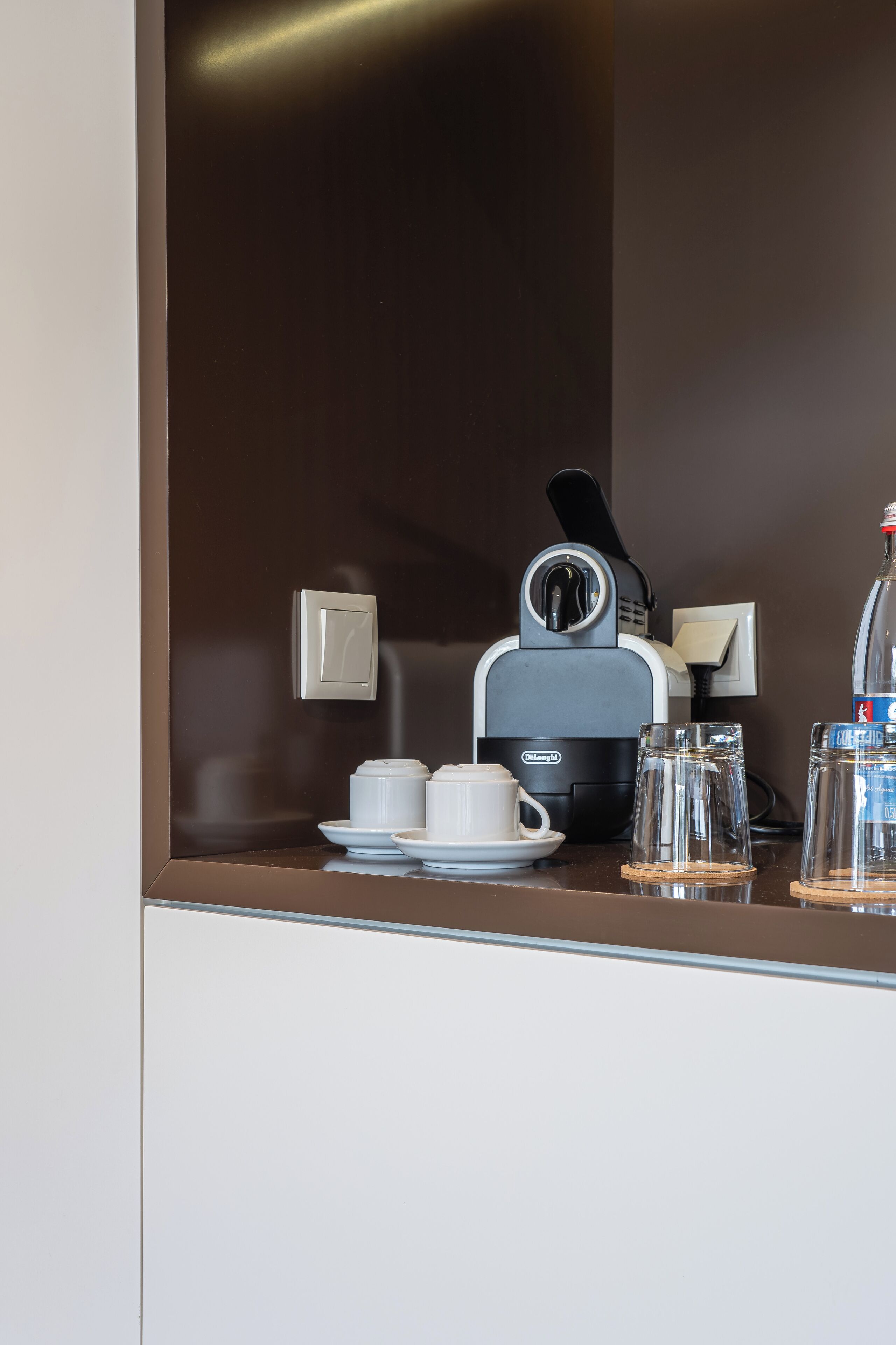 Eine Kaffeemaschine, zwei Tassen, ein Glas und eine Flasche auf einer Arbeitsplatte.