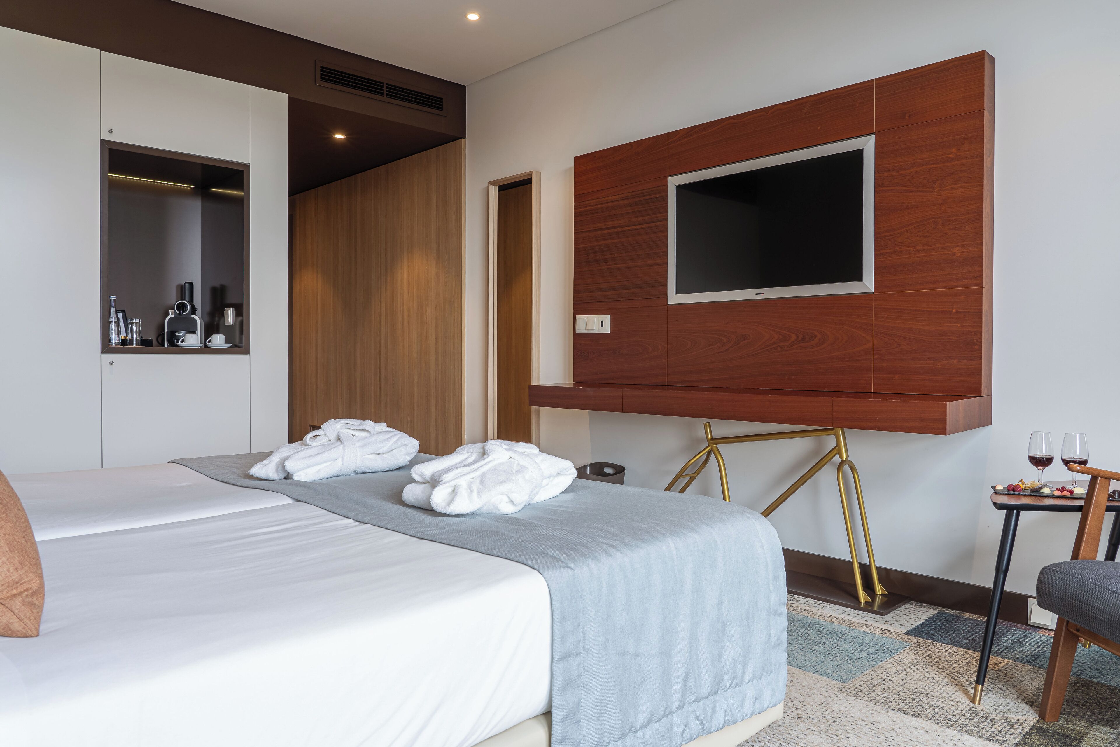 Une chambre d’hôtel avec un lit, un téléviseur fixé au mur, une petite table avec des verres et un meuble-miroir.