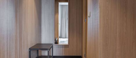 A hallway with wooden walls and a wooden floor, leading to a room with a bed and a window with curtains.