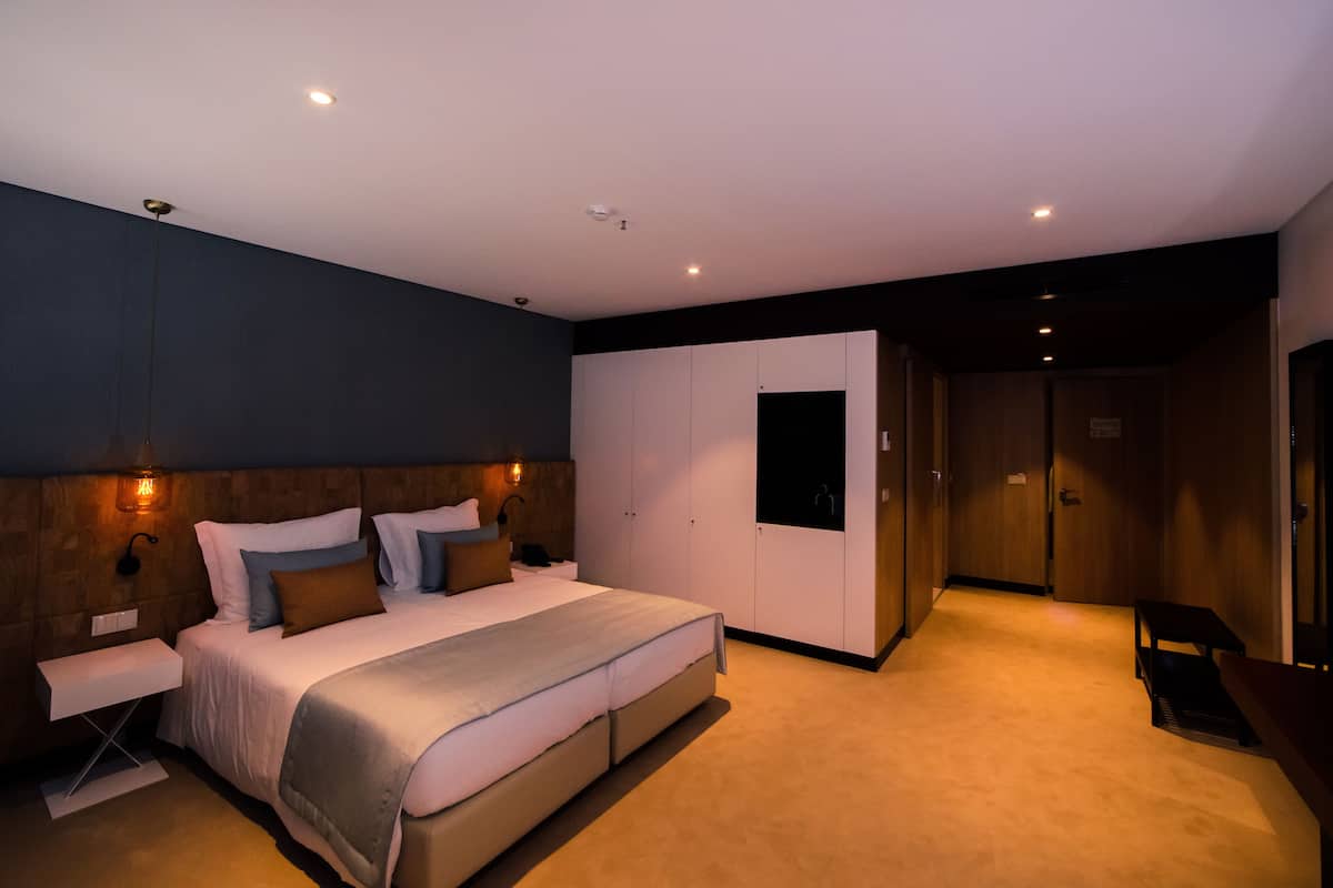 A modern bedroom with a large bed, bedside tables, a wardrobe, and a bench.