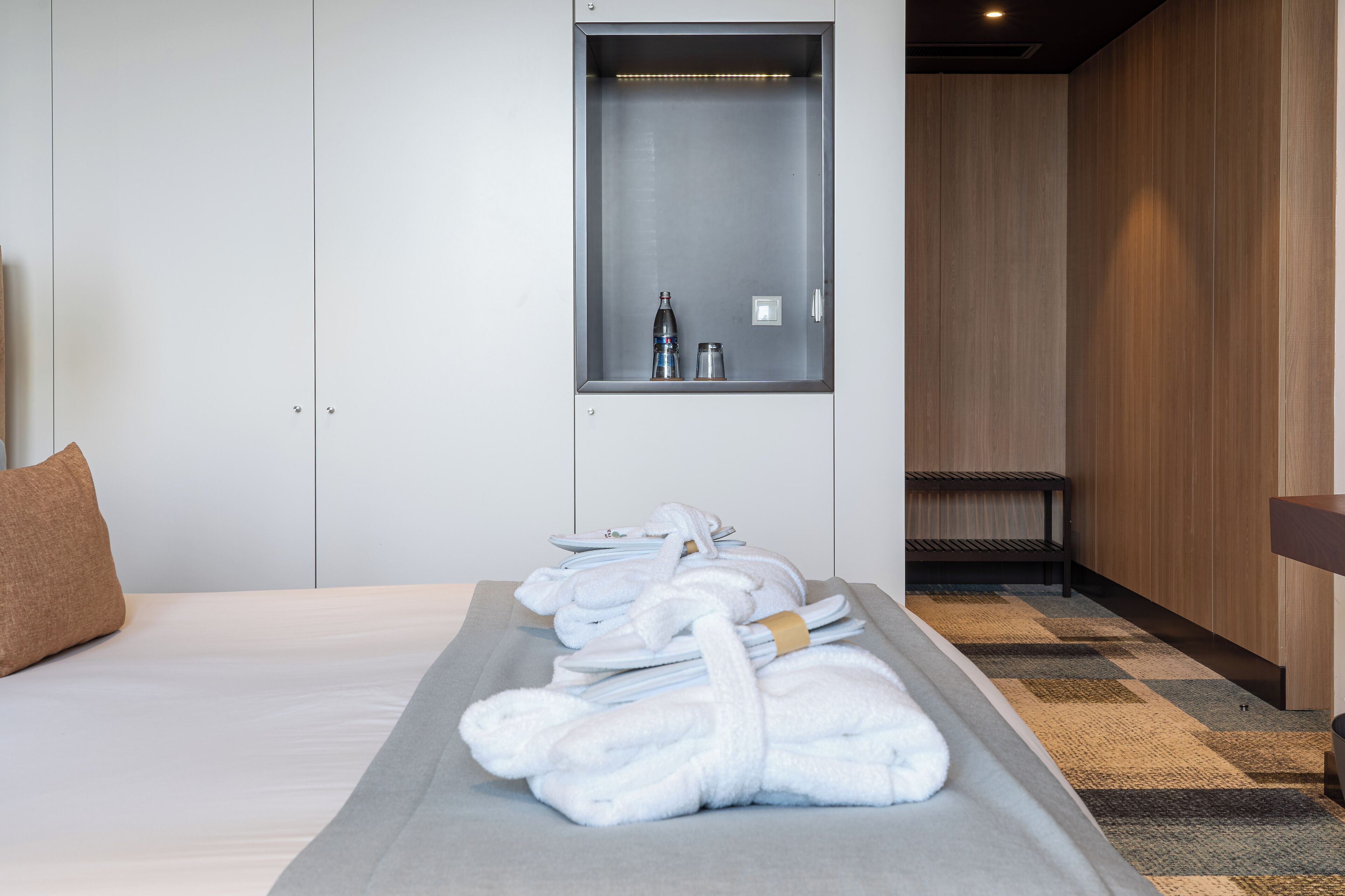 Habitación de hotel con una cama bien hecha, un pequeño espacio para sentarse y un mueble empotrado con artículos de aseo.