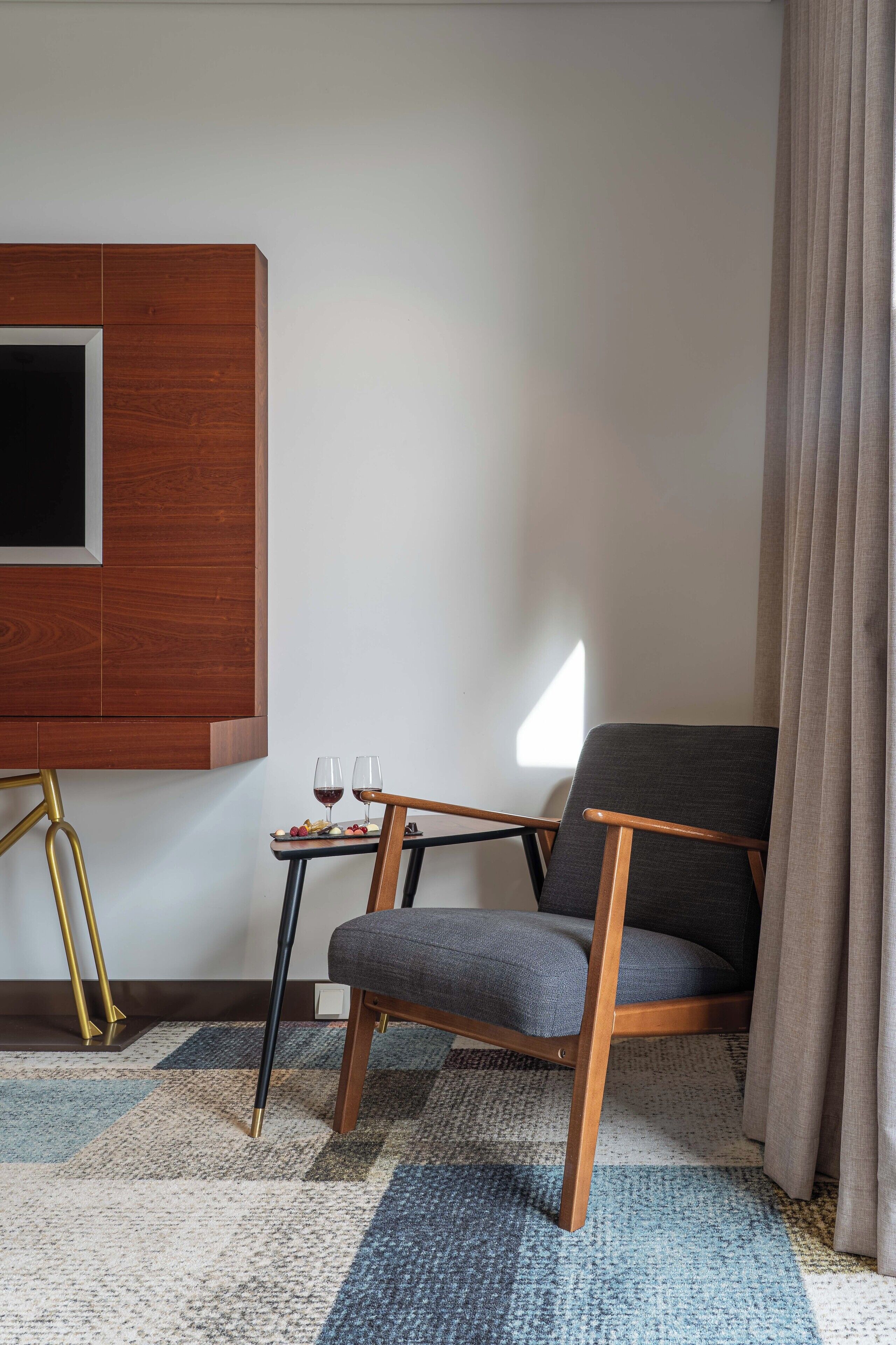 A modern room with a dark grey armchair, a small table with two glasses of red wine, and a wooden panel on the wall.