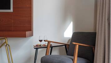 A modern room with a dark grey armchair, a small table with two glasses of red wine, and a wooden panel on the wall.