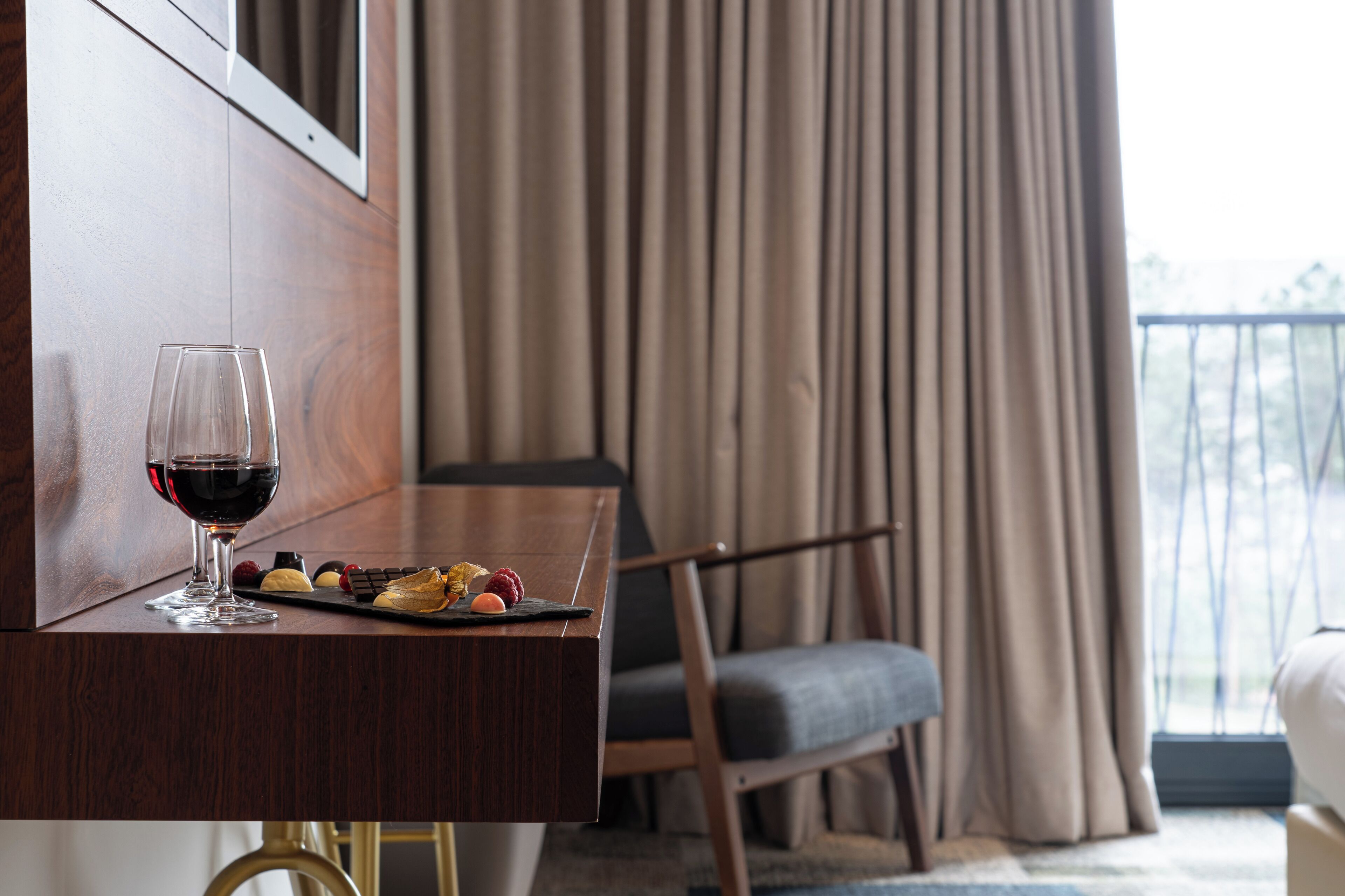 Una habitación de hotel con un escritorio de madera, una copa de vino tinto y una bandeja de pequeños bocadillos.