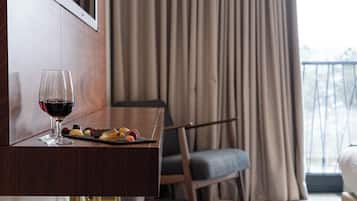 Una habitación de hotel con un escritorio de madera, una copa de vino tinto y una bandeja de pequeños bocadillos.