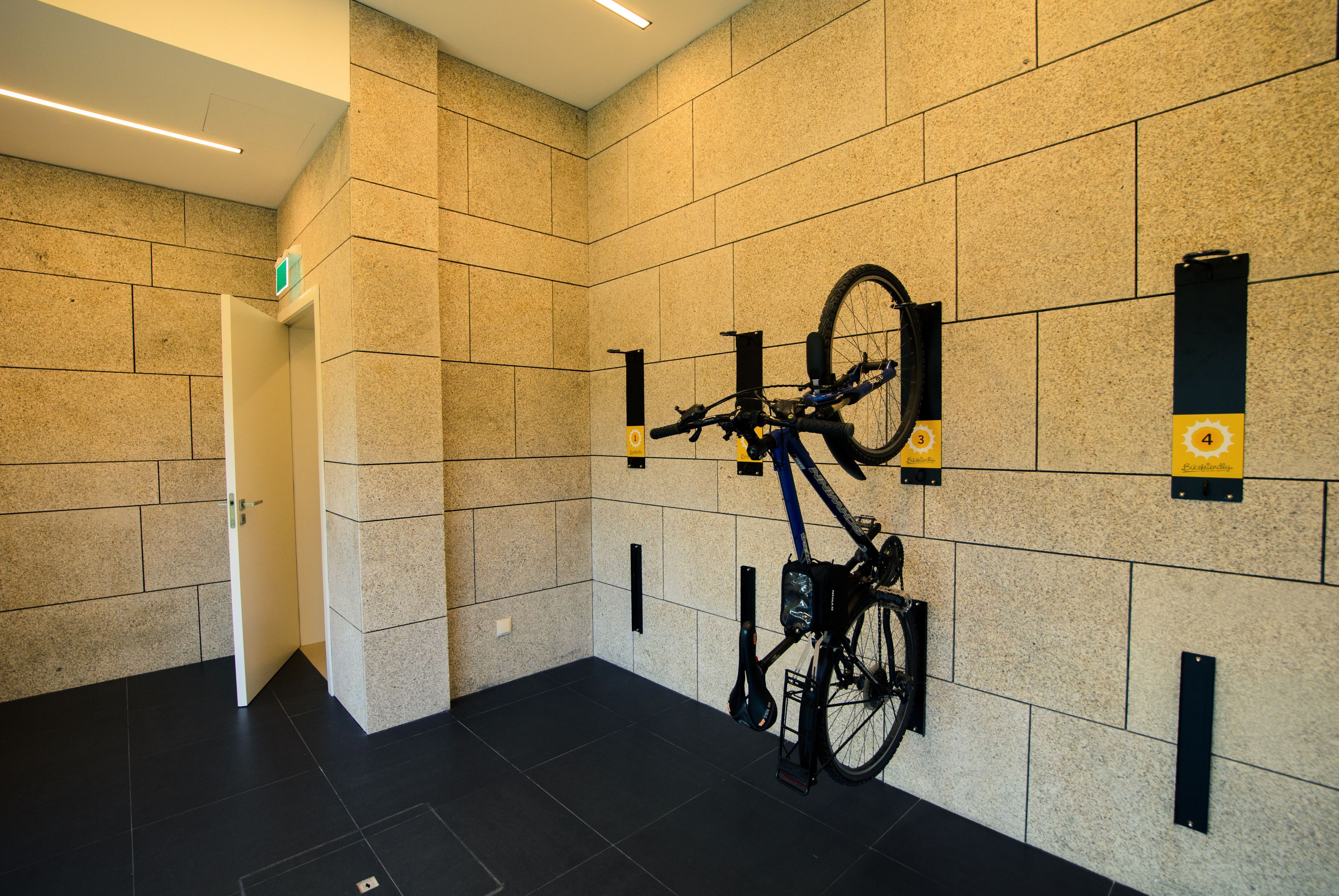 Un moderno vestíbulo de hotel con un soporte para bicicletas en la pared, una puerta que da a una habitación y un suelo limpio de baldosas.