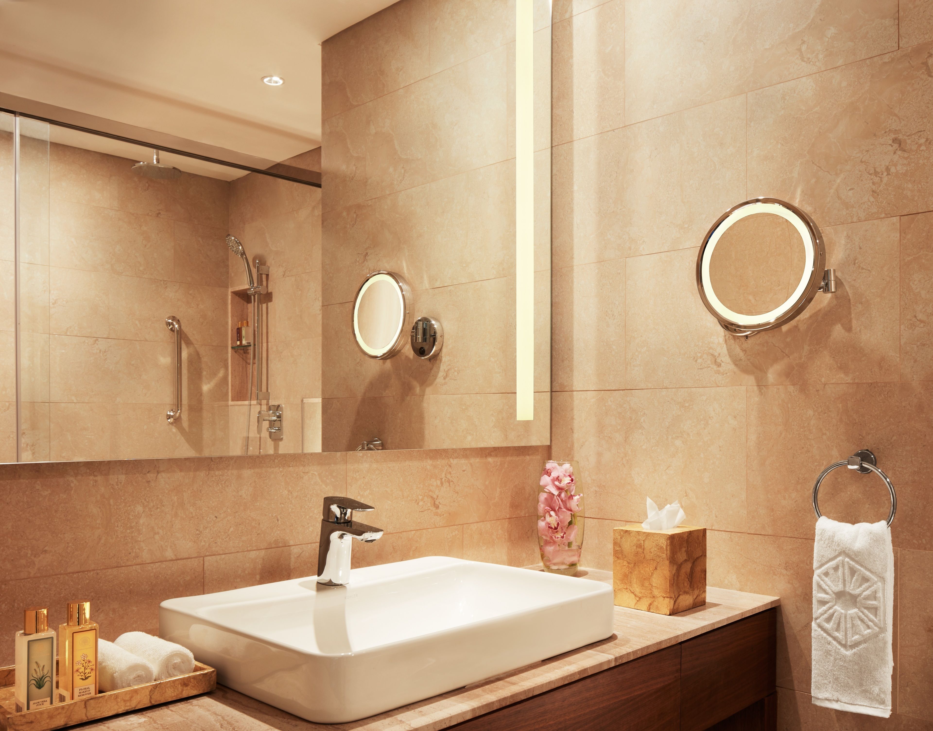 Un baño moderno con un lavamanos grande y rectangular, un cabezal de ducha de mano, un perchero y un espejo con marco circular.