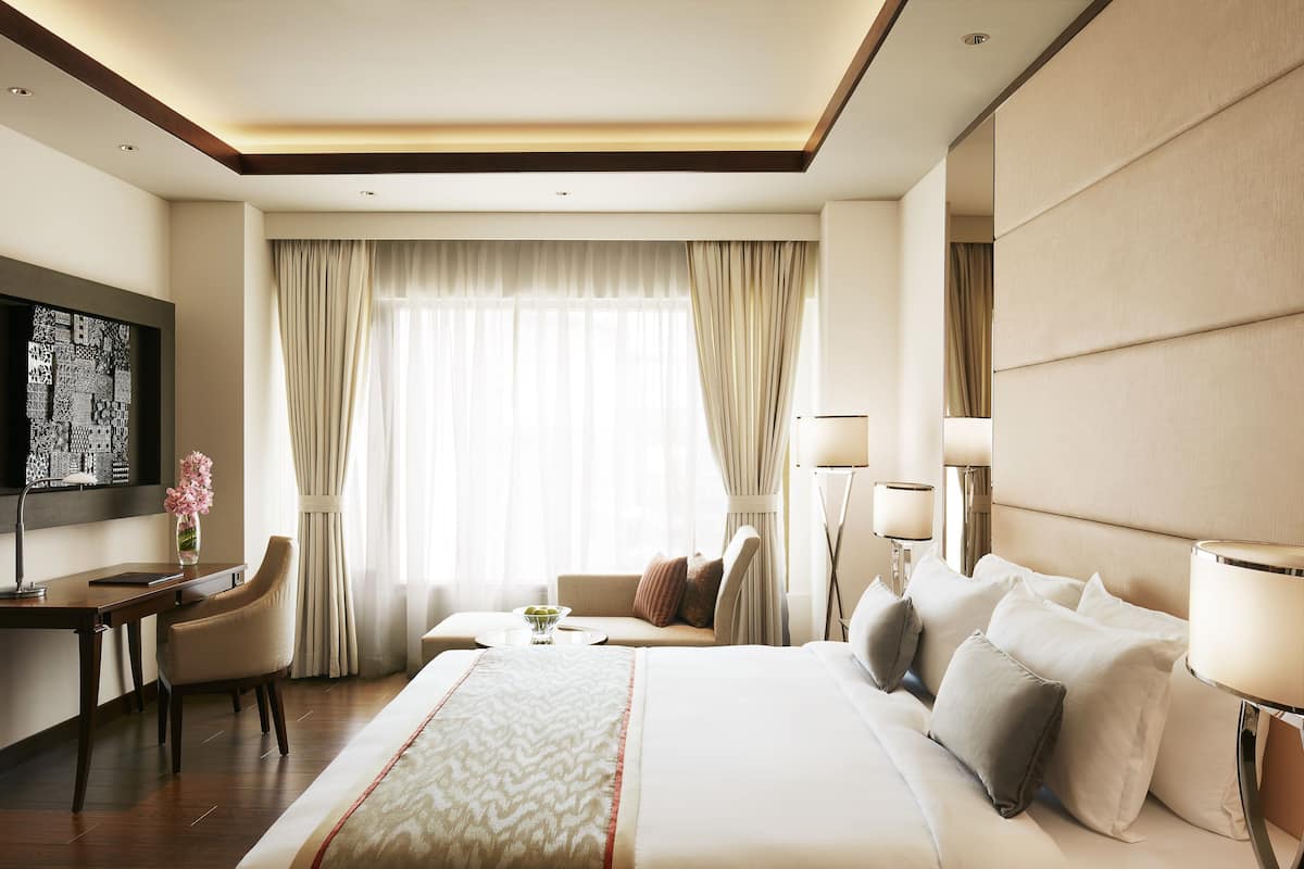 Habitación de hotel con una cama grande, un escritorio, una silla, un televisor y una ventana con cortinas.
