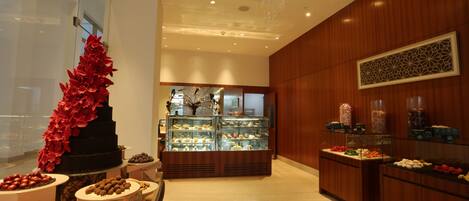A hotel lobby with a central display case, a decorative red floral arrangement, and various food displays.
