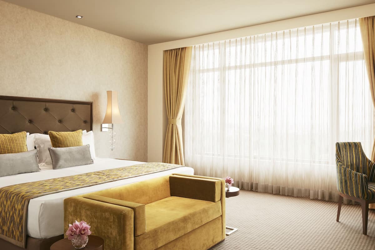 Quarto de hotel com uma cama grande, um sofá, uma poltrona e uma janela com cortinas.