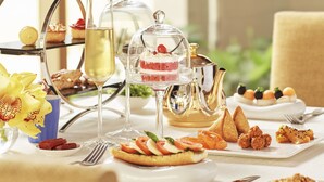 Una mesa servida con diversos alimentos, entre ellos pasteles, una copa de vino y un hervidor de té.