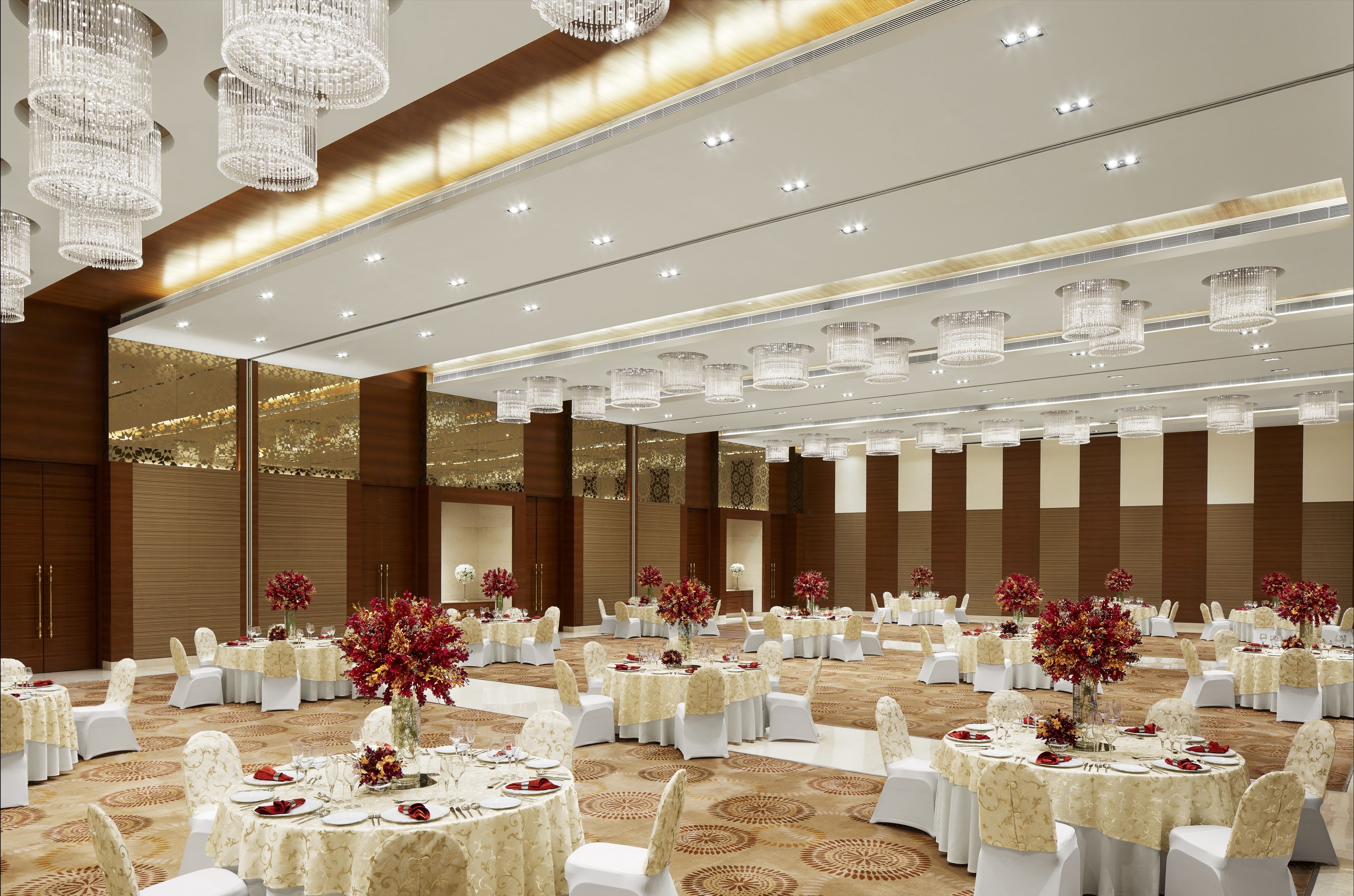 Une grande salle de banquet avec des tables rondes, des chaises blanches et des lustres.