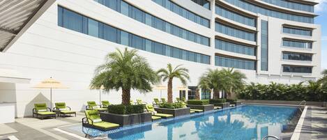 A modern hotel with a large indoor swimming pool, sun loungers, and palm trees.