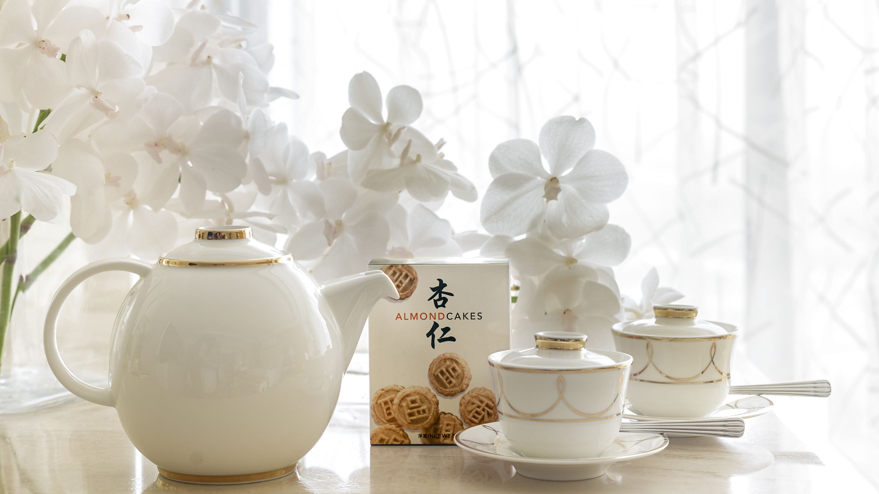 A tea set with a teapot, cups, and saucers, accompanied by a box of almond cakes.