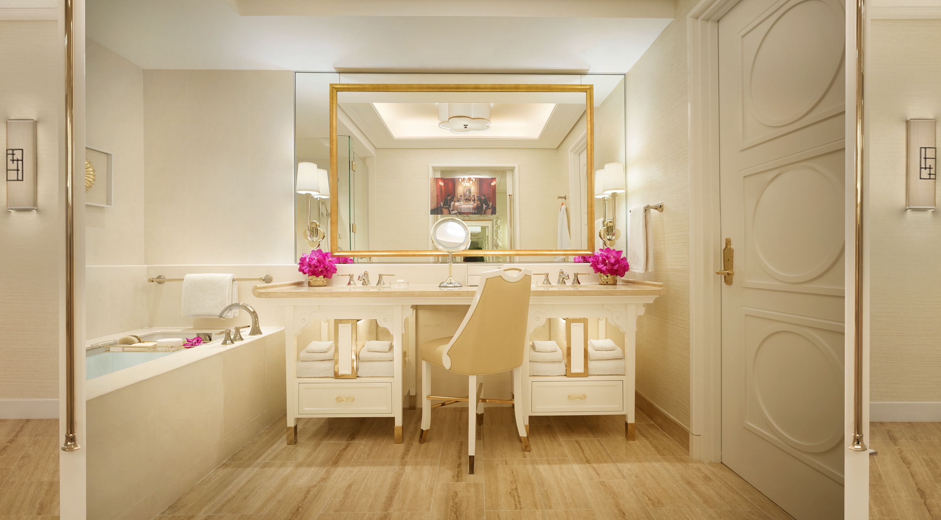 Un baño lujoso con un espejo grande, dos lavamanos, una bañera y una silla de tocador.