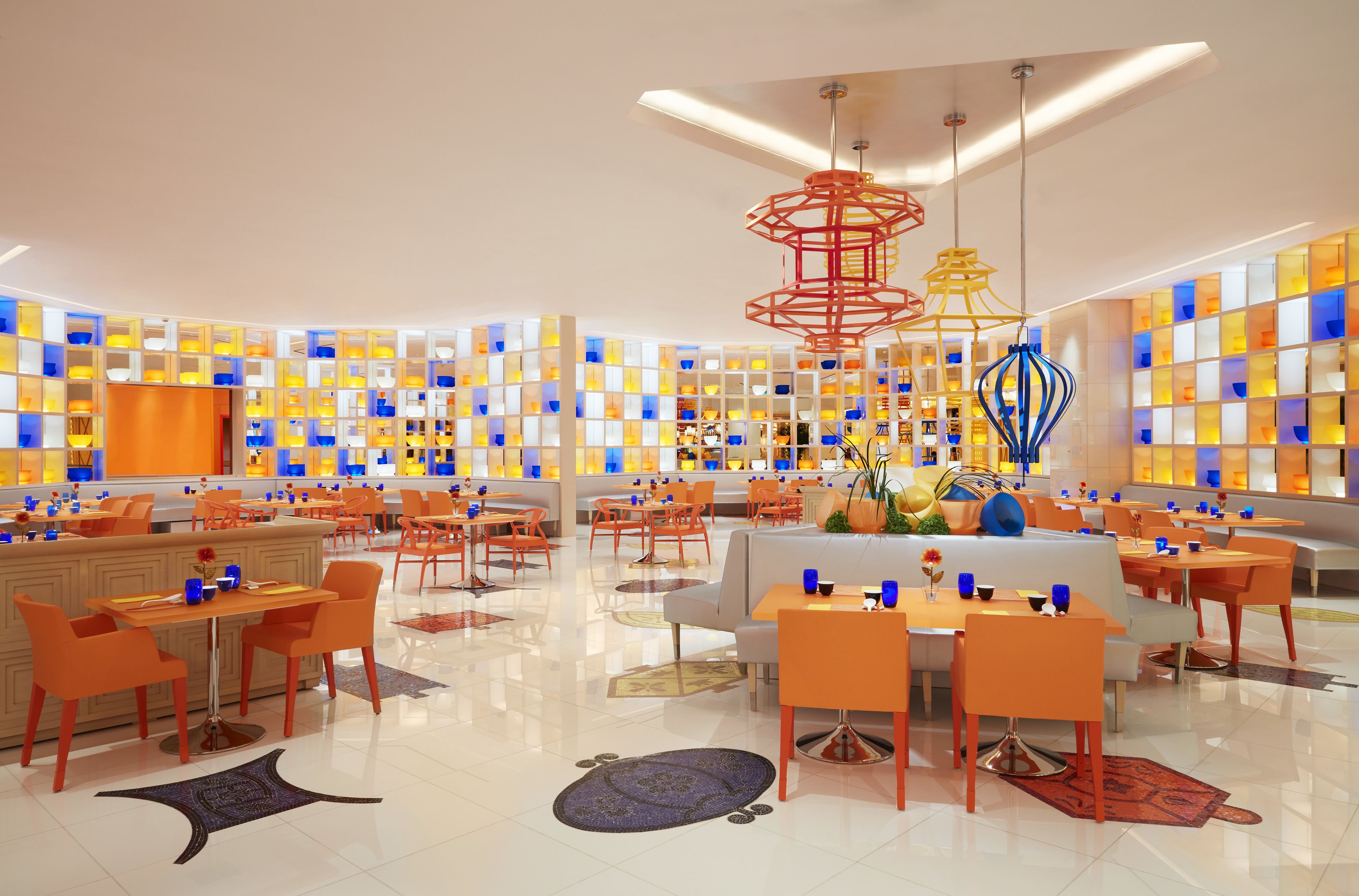 A modern hotel lobby with a central seating area, multiple dining tables, and a vibrant wall display.