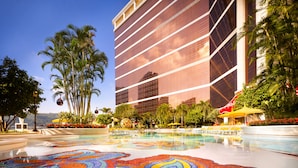 A hotel pool area with a colorful mosaic floor, palm trees, and a modern building in the background. - Wynn Palace (Cotai)