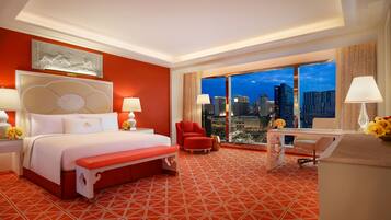 A hotel room with a large bed, a red armchair, a desk, and a view of the cityscape at night.