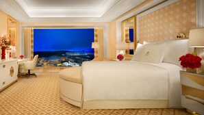 A luxurious hotel room with a large bed, a desk, and a view of a cityscape at night. - Wynn Palace (Cotai)