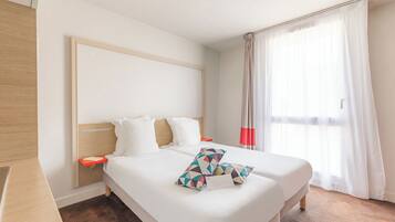 A hotel room with a large bed, a wooden headboard, a bedside table, and a window with sheer curtains.