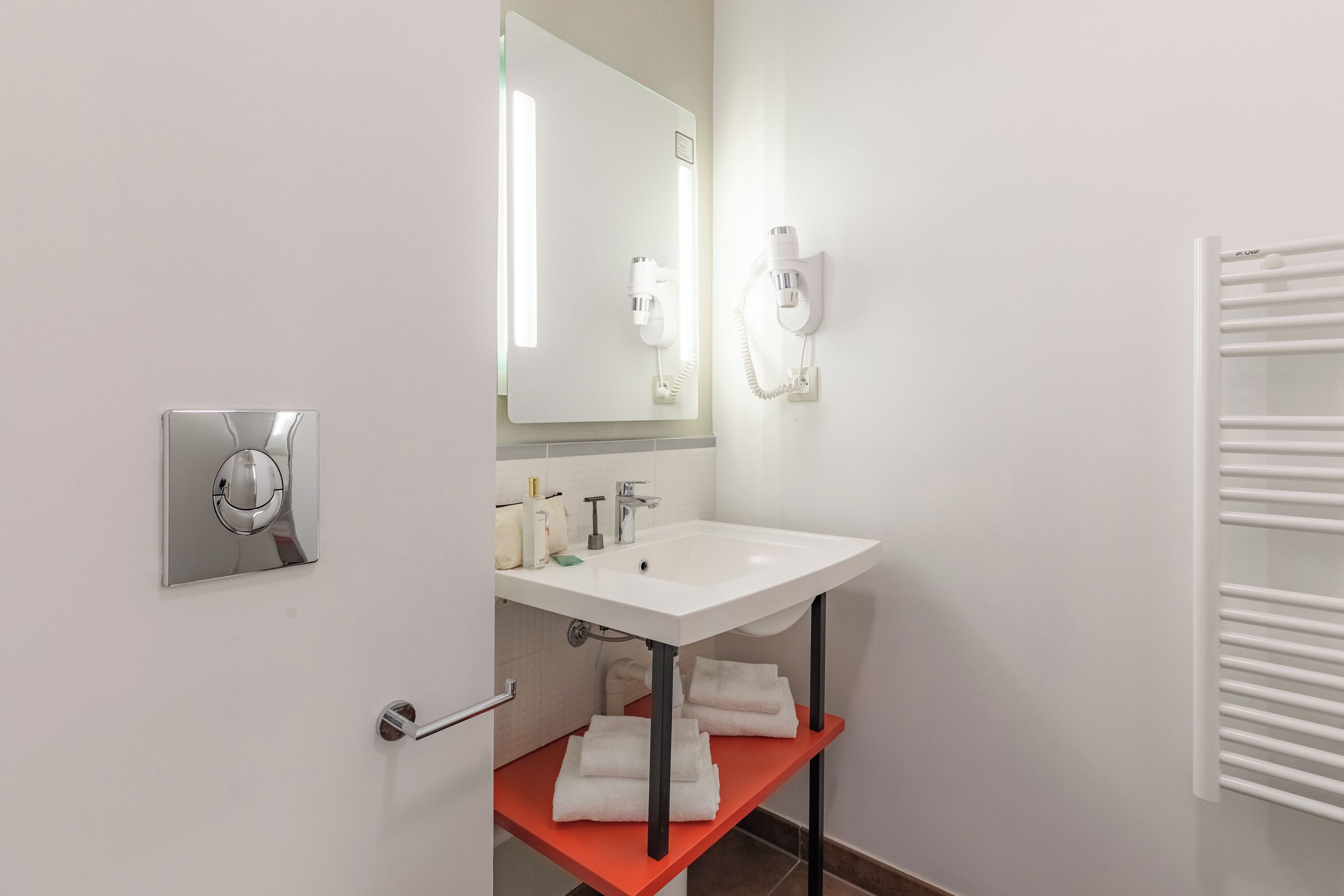 Een moderne badkamer met een witte wasbak, een spiegel, een haardroger en een handdoekhouder.