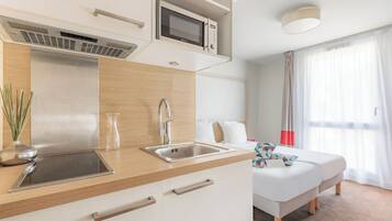 Una habitación de hotel moderna con kitchenette, una cama y un amplio ventanal con cortinas.