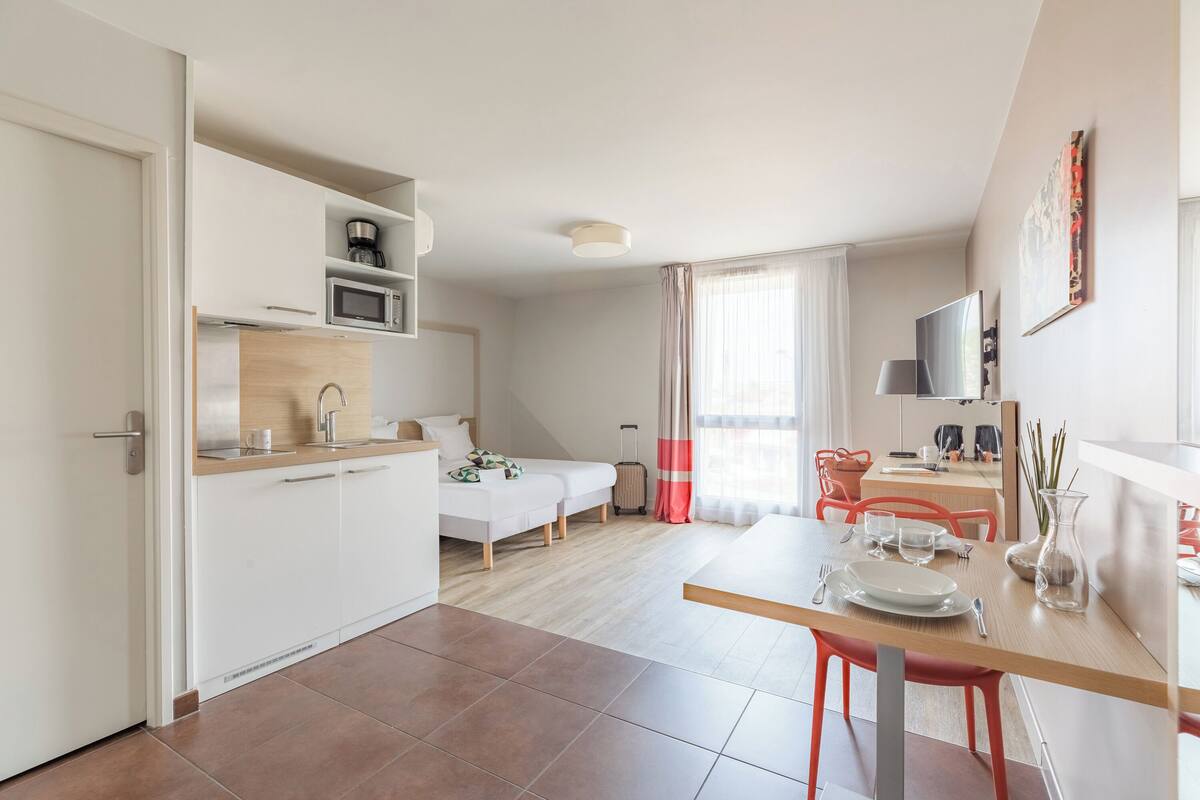 Een moderne hotelkamer met kitchenette, eethoek, bed en badkamer.