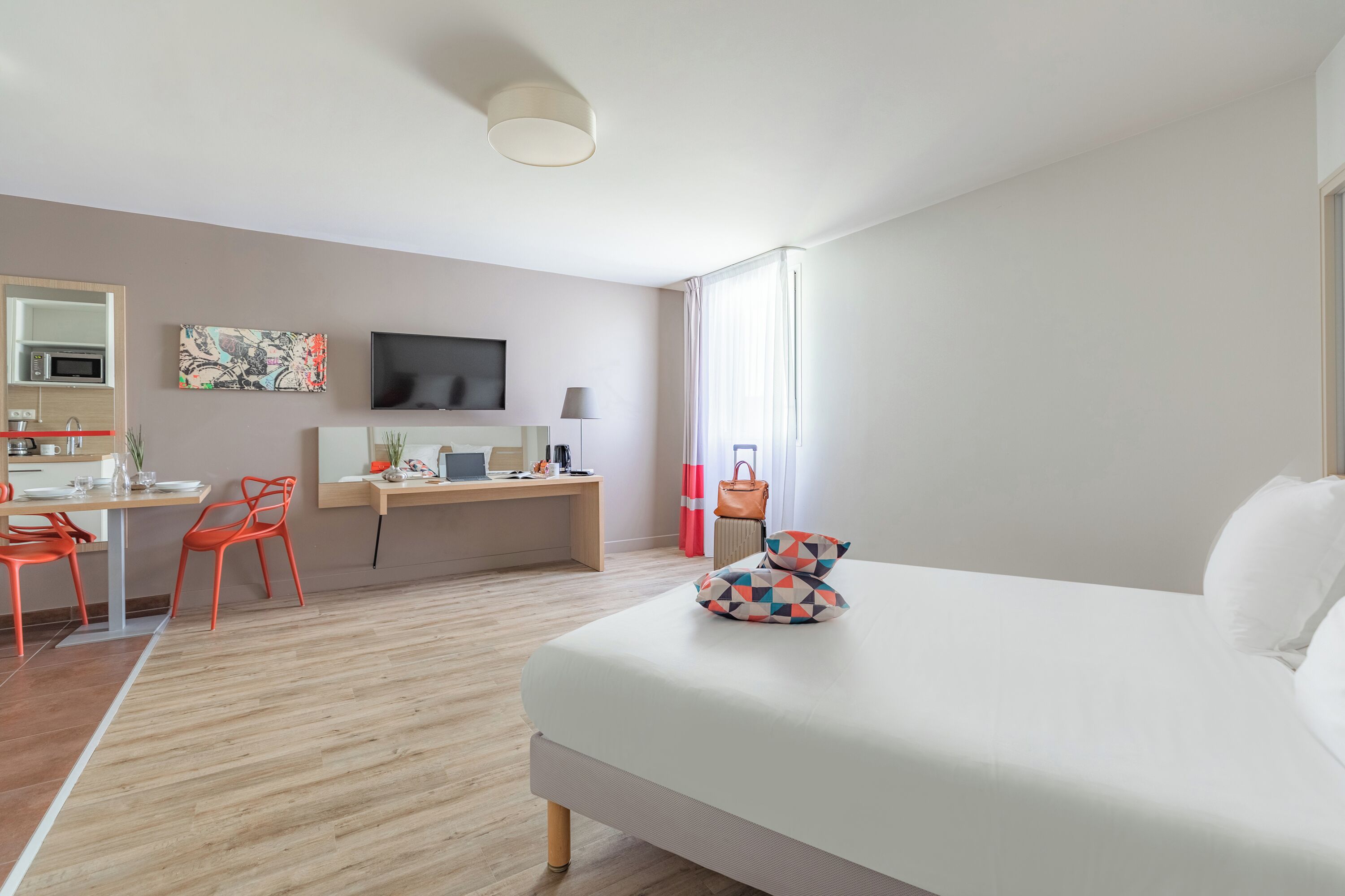 Habitación de hotel moderna con cama, escritorio, silla, televisión y vistas al exterior.