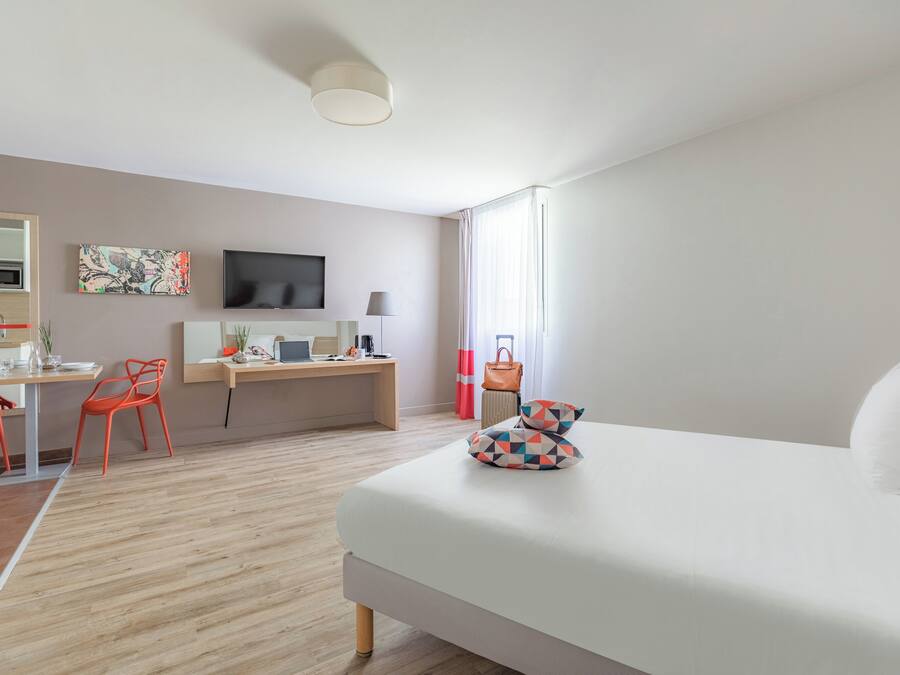 Habitación de hotel moderna con cama, escritorio, silla, televisión y vistas al exterior.