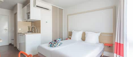 A hotel room with a bed, a small kitchenette, a chair, and a bathroom.