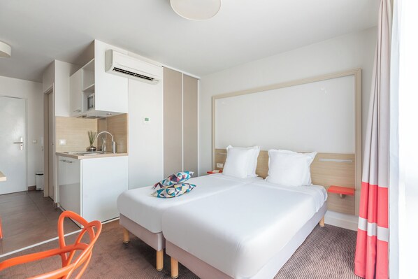 Una habitación de hotel con cama, kitchenette pequeña, una silla y baño.