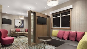 Una habitación de hotel moderna con sofá modular, una mesa redonda, un sillón rojo, un ventanal grande y un televisor de pantalla plana montado en la pared.