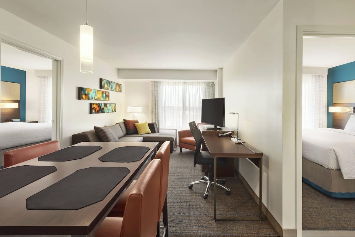 Ein Hotelzimmer mit Bett, Schreibtisch, Sessel, Sofa und Fernseher.
