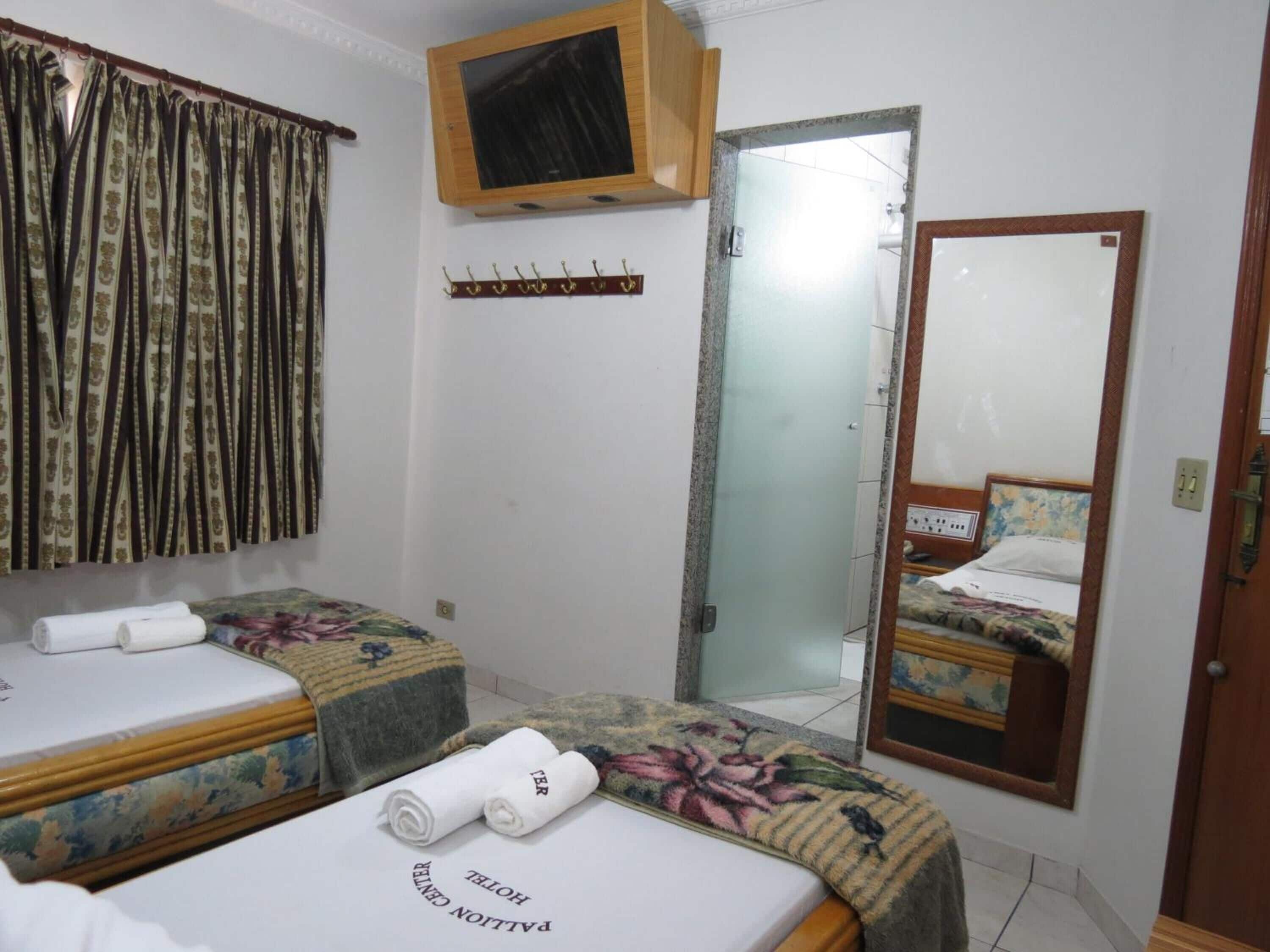 A hotel room with two beds, a television, a mirror, and a window with curtains.