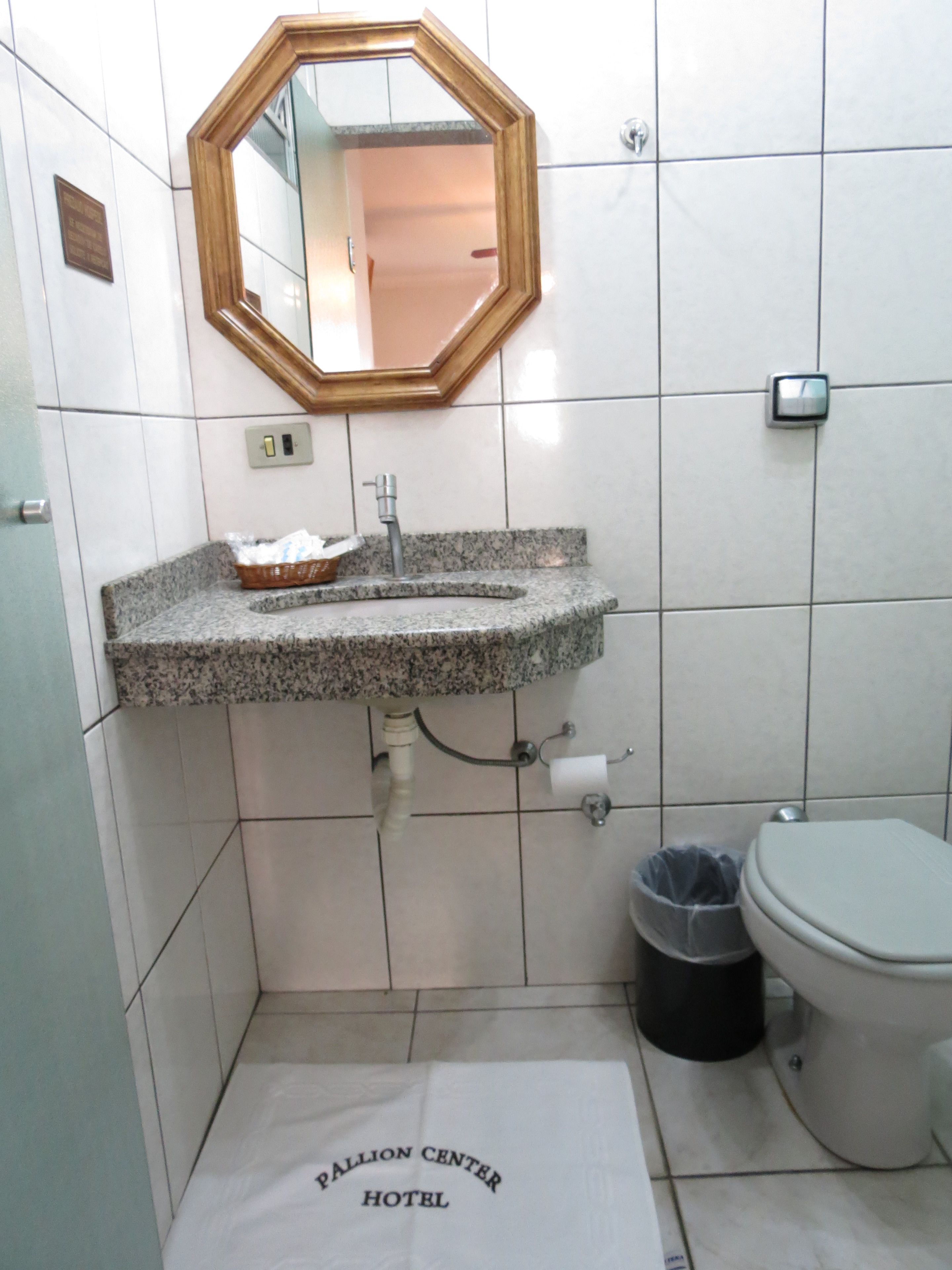 Un baño con lavamanos de granito, un espejo, un inodoro y un cubo de basura.