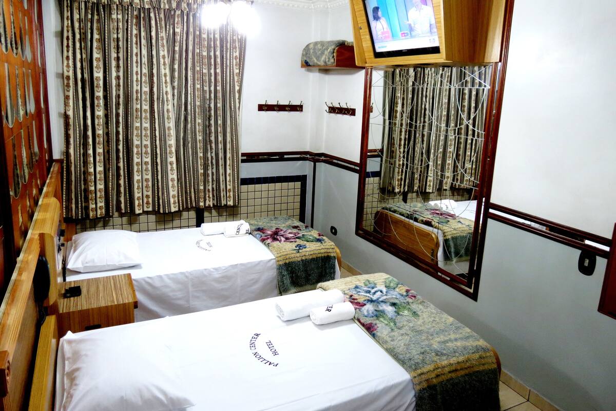 A hotel room with two beds, a television mounted on the wall, and a mirror reflecting part of the room.