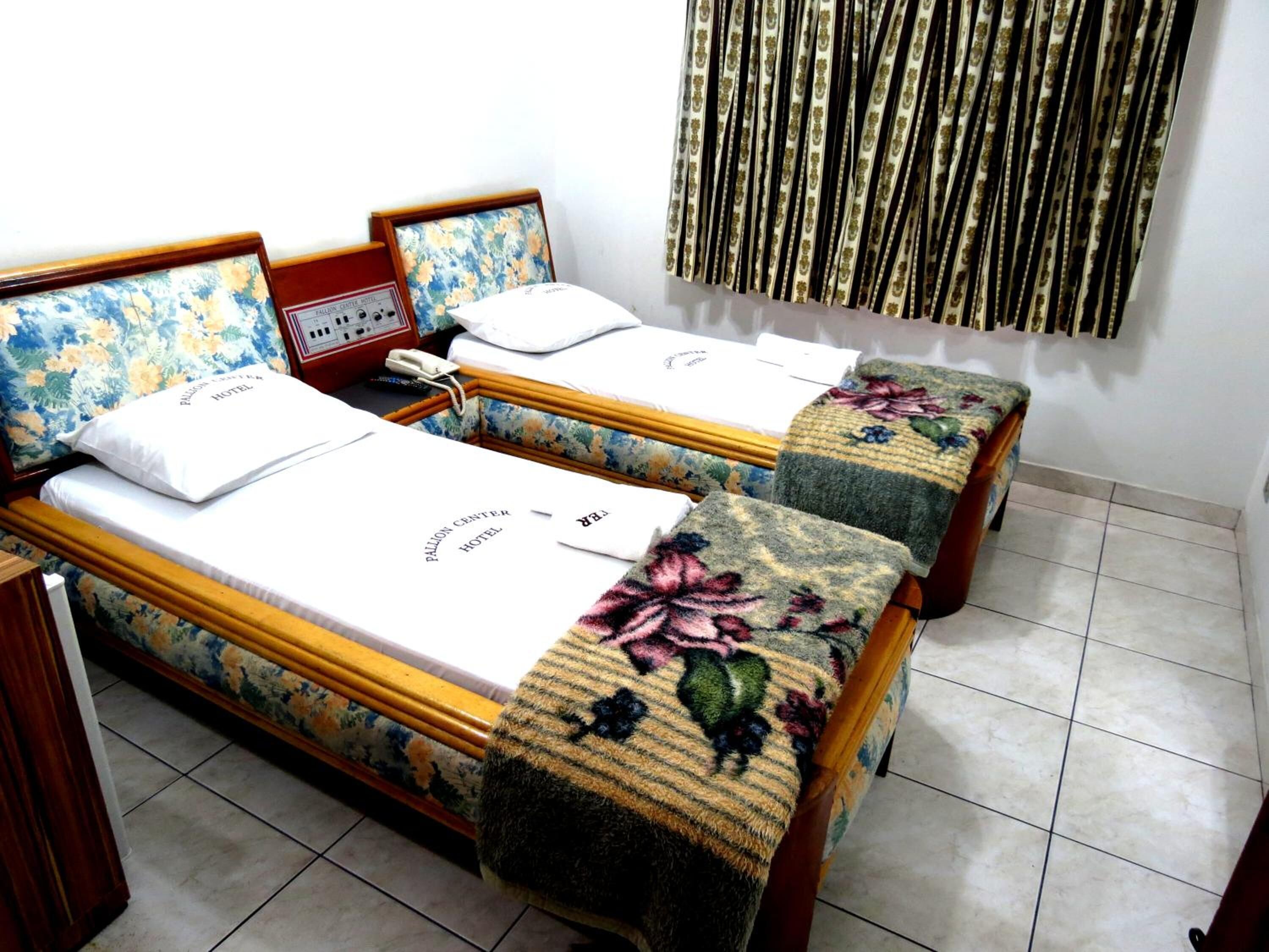 A hotel room with two beds, floral headboards, a bedside table with a telephone, and a curtain with a vertical pattern.
